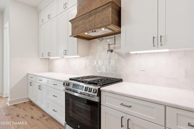 kitchen featuring gas range, custom exhaust hood, white cabinets, and backsplash