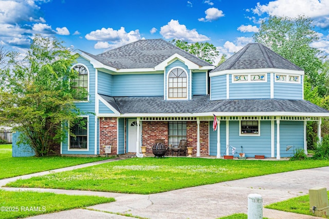 view of front of house with covered porch, a shingled roof, a front lawn, and brick siding