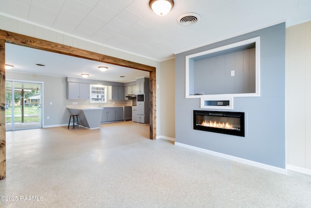 unfurnished living room with baseboards, visible vents, light speckled floor, and a glass covered fireplace