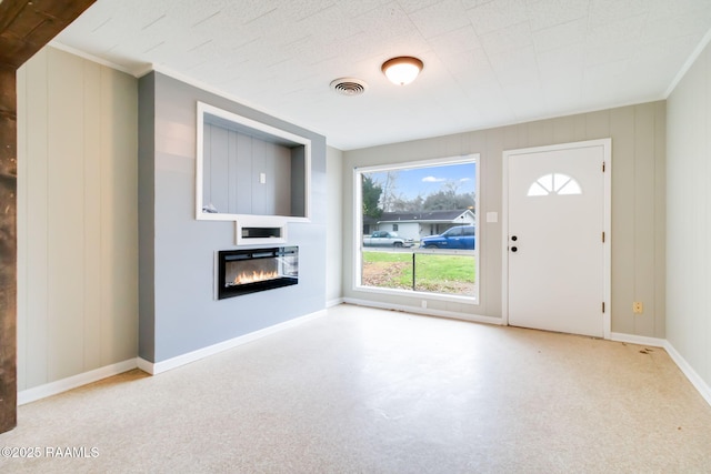 unfurnished living room with ornamental molding, a glass covered fireplace, visible vents, and baseboards