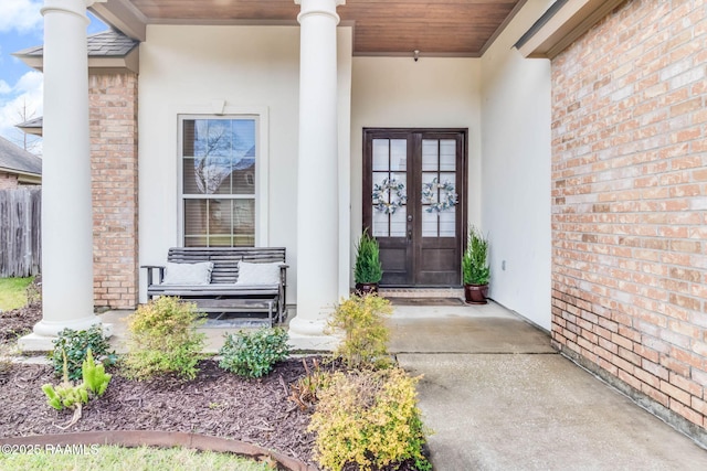 view of exterior entry featuring french doors, brick siding, a porch, and stucco siding