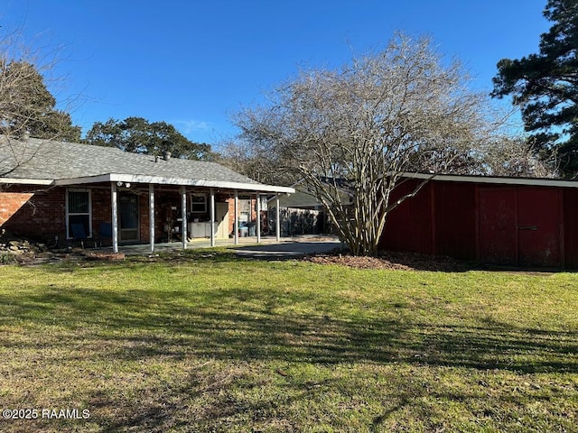 back of property featuring a yard, brick siding, an outbuilding, and a patio