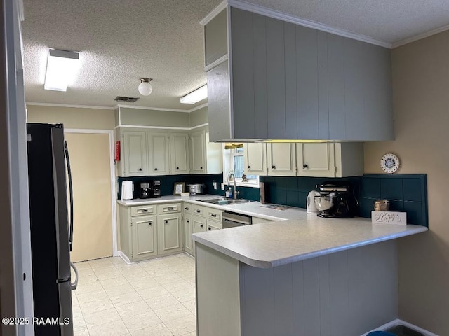 kitchen featuring crown molding, light countertops, freestanding refrigerator, a sink, and a peninsula