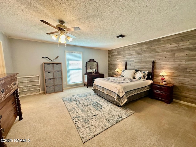 carpeted bedroom featuring a textured ceiling, wood walls, visible vents, a ceiling fan, and ornamental molding