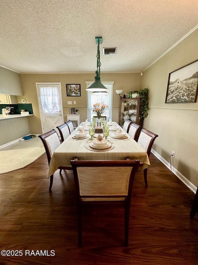 dining space featuring baseboards, wood finished floors, visible vents, and crown molding