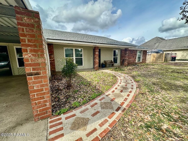 view of front facade with a shingled roof, fence, and brick siding