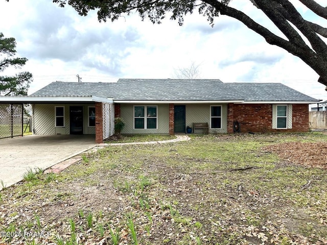 ranch-style home with driveway, an attached carport, roof with shingles, and brick siding