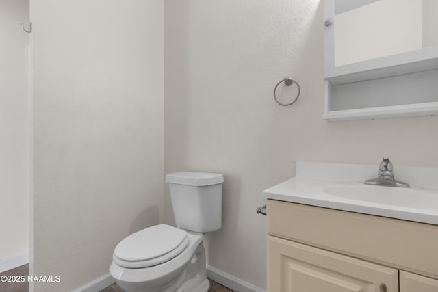 half bath featuring toilet, baseboards, and vanity