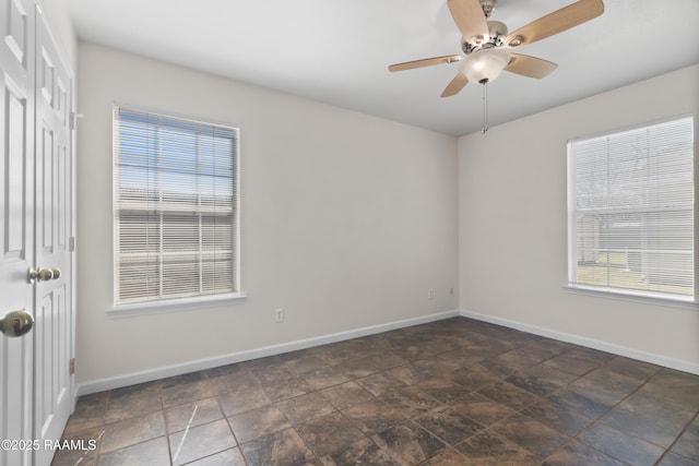 spare room with ceiling fan, stone finish floor, and baseboards