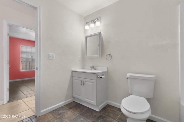 half bath featuring baseboards, a textured wall, vanity, and toilet