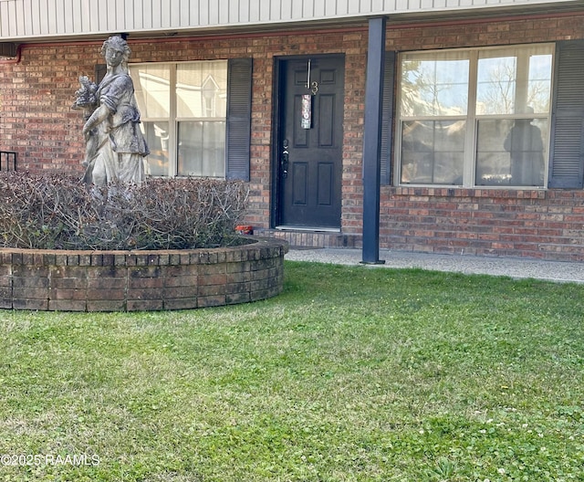 view of exterior entry with board and batten siding, a lawn, and brick siding