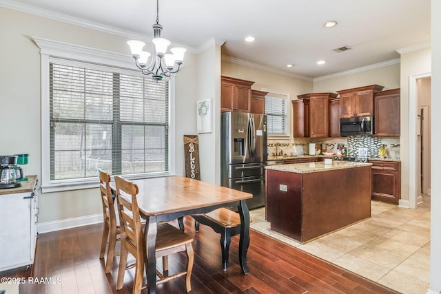 kitchen featuring stainless steel appliances, a kitchen island, visible vents, backsplash, and decorative light fixtures