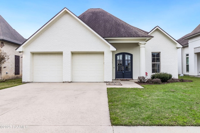 view of front facade with a shingled roof, concrete driveway, an attached garage, french doors, and a front lawn