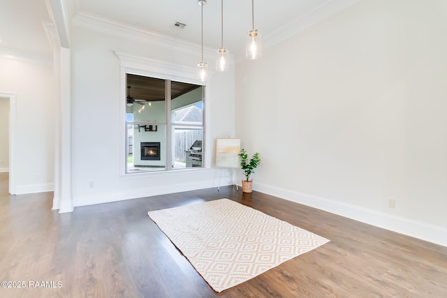 unfurnished dining area with dark wood-type flooring, visible vents, baseboards, a glass covered fireplace, and crown molding