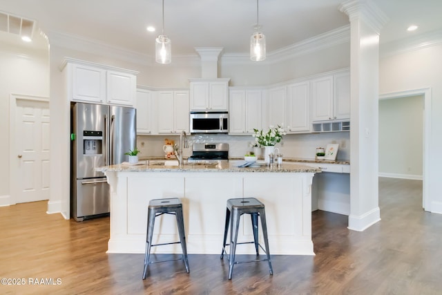 kitchen with stainless steel appliances, a kitchen island with sink, white cabinetry, and light stone counters