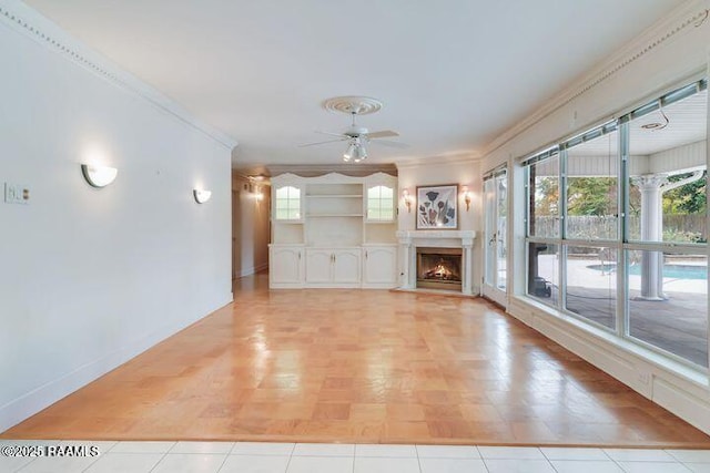 unfurnished living room featuring crown molding, baseboards, a lit fireplace, and ceiling fan