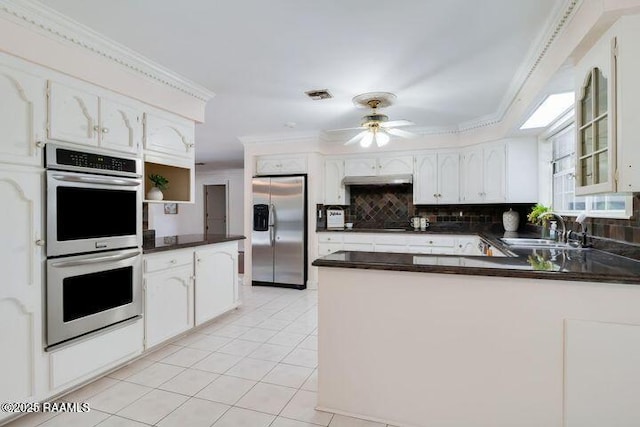 kitchen featuring a peninsula, a sink, ornamental molding, stainless steel appliances, and dark countertops