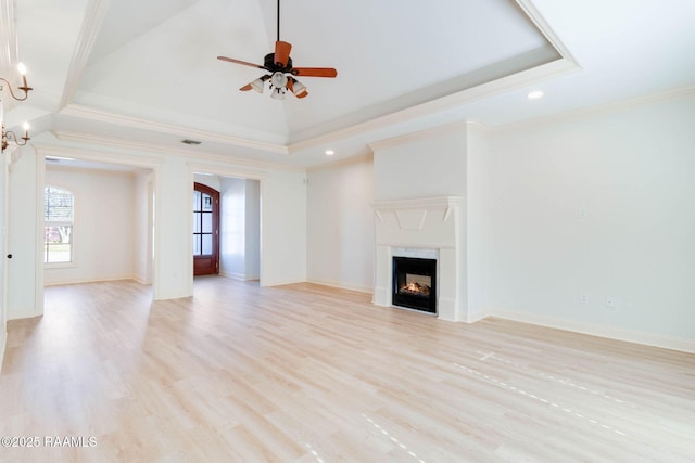 unfurnished living room featuring a warm lit fireplace, a raised ceiling, crown molding, and light wood-style flooring