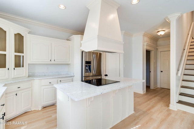 kitchen featuring light stone counters, a center island, premium range hood, white cabinetry, and stainless steel refrigerator with ice dispenser