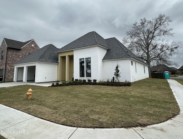 french country style house with driveway, a garage, brick siding, roof with shingles, and a front yard