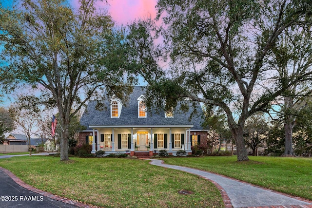 new england style home featuring a porch, roof with shingles, and a yard