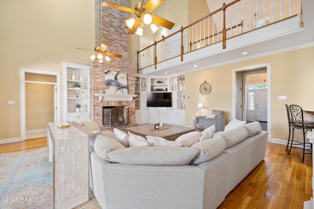 living area with baseboards, wood finished floors, a high ceiling, a brick fireplace, and built in shelves