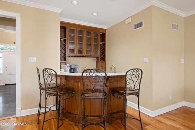 bar featuring baseboards, wood finished floors, visible vents, and crown molding