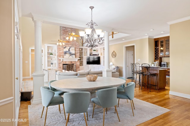 dining room with ornamental molding, a brick fireplace, light wood finished floors, and ornate columns