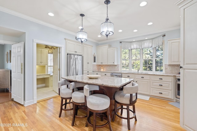 kitchen featuring light wood finished floors, a breakfast bar area, stainless steel appliances, and ornamental molding