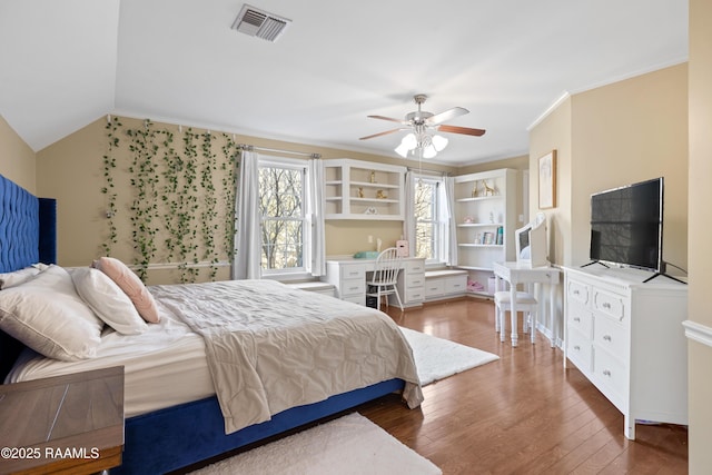 bedroom featuring visible vents, built in study area, hardwood / wood-style flooring, vaulted ceiling, and crown molding