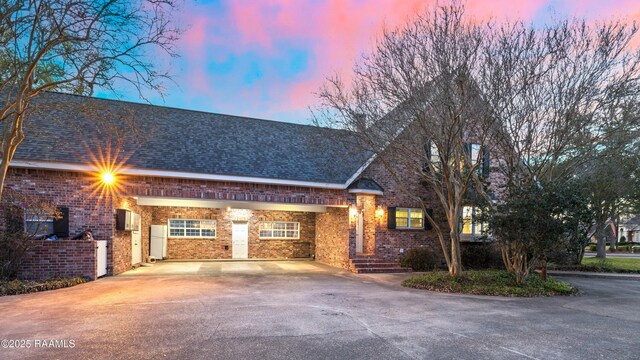 view of front facade featuring driveway, a shingled roof, an attached carport, and brick siding