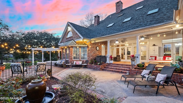 rear view of property featuring brick siding, a shingled roof, french doors, a chimney, and a patio area