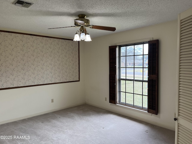 carpeted spare room with wallpapered walls, a textured ceiling, visible vents, and a wealth of natural light