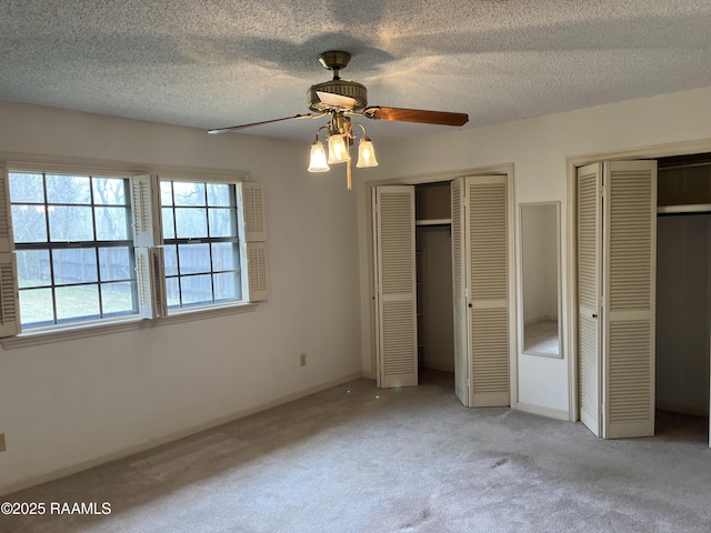 unfurnished bedroom with baseboards, a textured ceiling, light colored carpet, and multiple closets