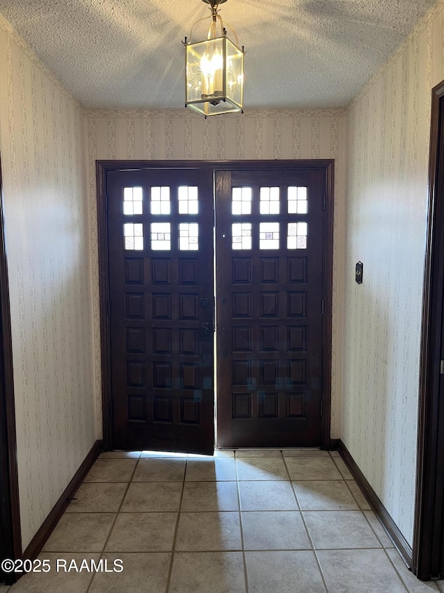 tiled entrance foyer with a textured ceiling, baseboards, and wallpapered walls