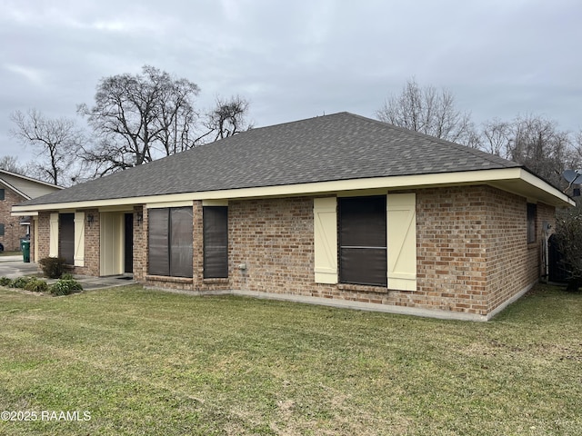 back of house with a shingled roof, brick siding, and a lawn