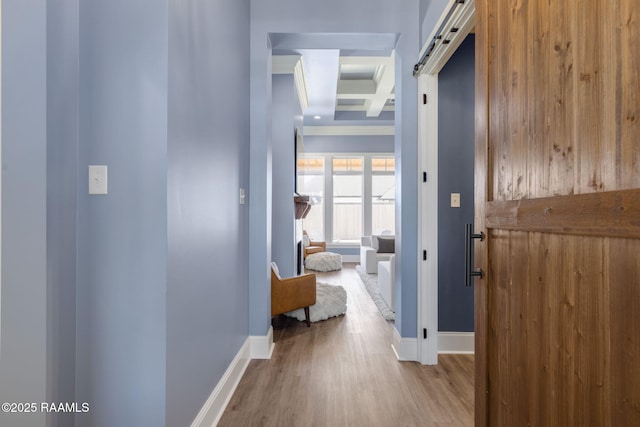 hallway featuring a barn door, coffered ceiling, wood finished floors, baseboards, and beamed ceiling