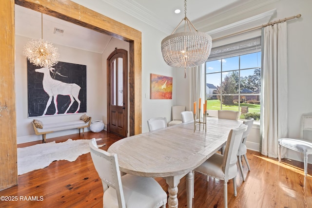 dining space with baseboards, visible vents, ornamental molding, wood finished floors, and an inviting chandelier