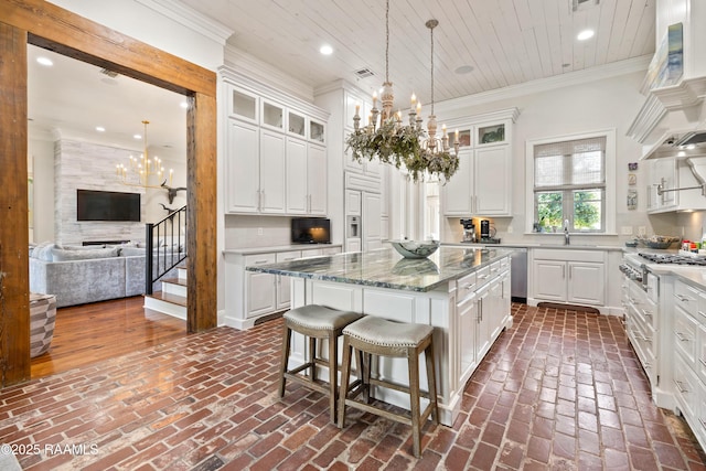 kitchen featuring brick floor, a center island, crown molding, a notable chandelier, and stainless steel appliances