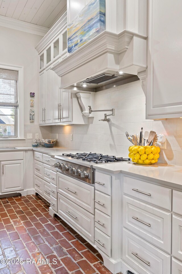 kitchen featuring brick floor, stainless steel gas stovetop, ornamental molding, and white cabinets