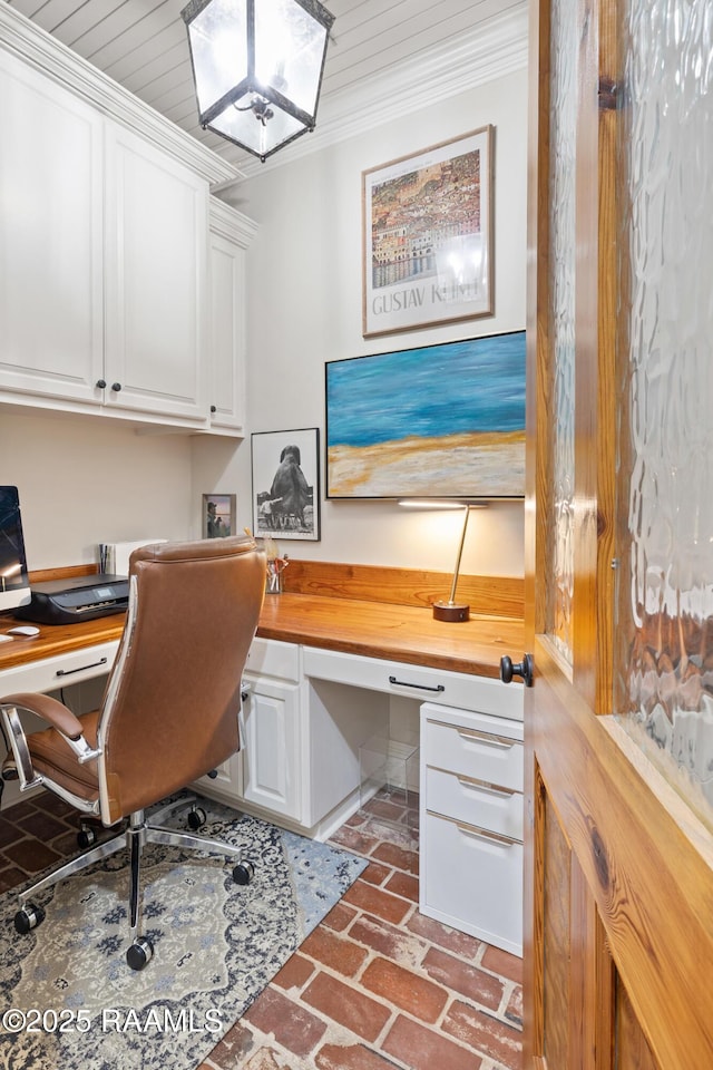 home office with ornamental molding, brick floor, and built in study area