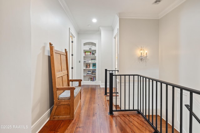 hallway with hardwood / wood-style flooring, an upstairs landing, baseboards, built in features, and crown molding