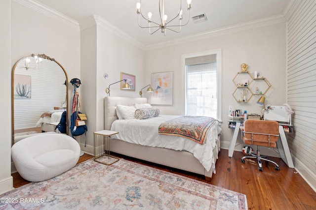 bedroom with wood finished floors, visible vents, baseboards, ornamental molding, and an inviting chandelier