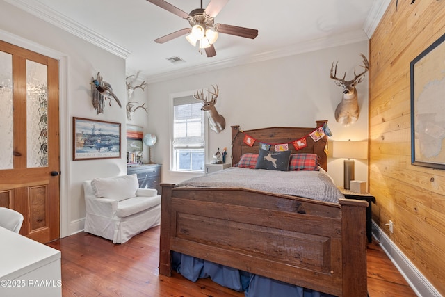 bedroom with crown molding, visible vents, a ceiling fan, wood walls, and wood finished floors