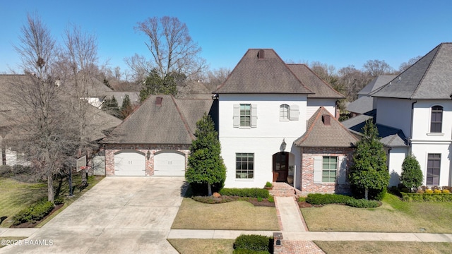 french provincial home featuring a garage, driveway, brick siding, and roof with shingles