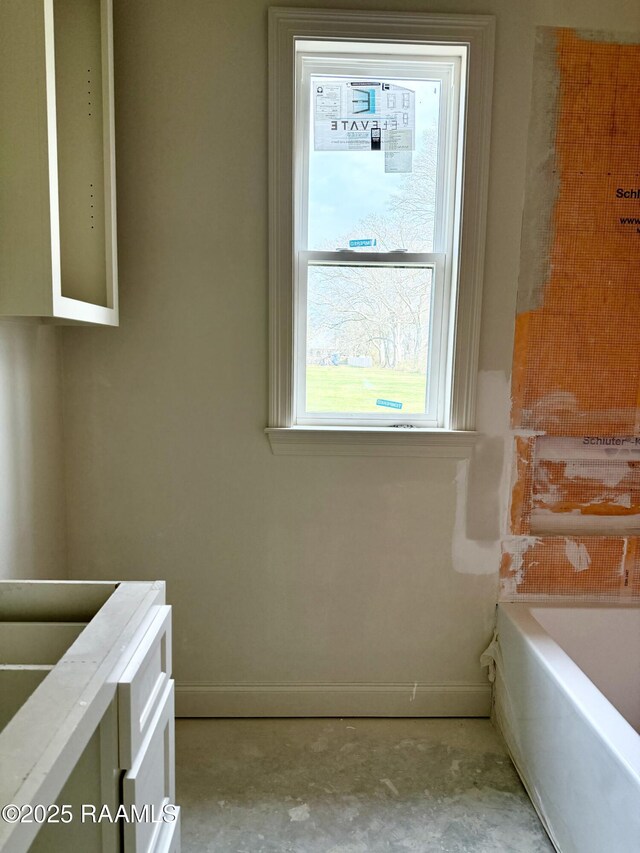 bathroom with unfinished concrete floors, a bathing tub, and baseboards