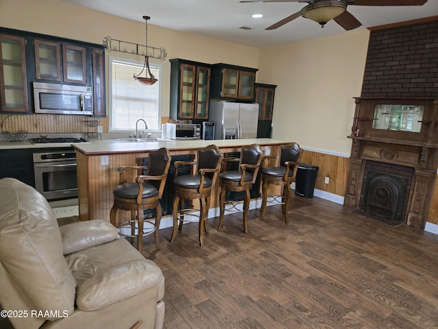 kitchen with appliances with stainless steel finishes, glass insert cabinets, light countertops, pendant lighting, and a sink