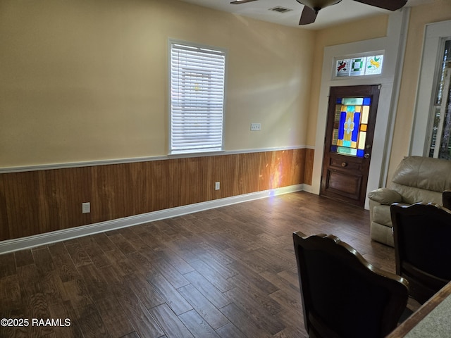 unfurnished living room featuring visible vents, a ceiling fan, wainscoting, dark wood-type flooring, and wood walls