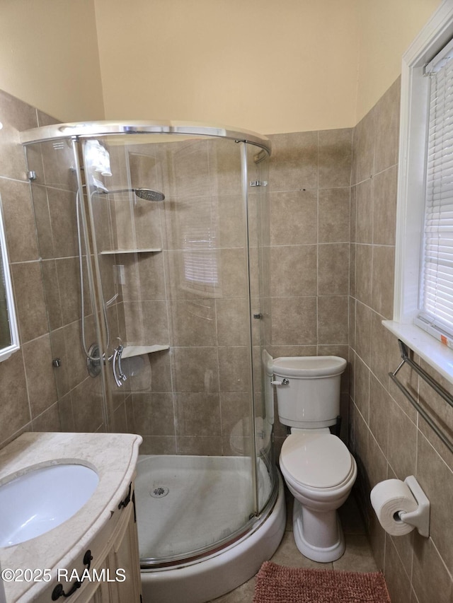 bathroom featuring tile walls, toilet, a stall shower, vanity, and tile patterned floors