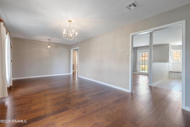 empty room with dark wood-style floors, visible vents, baseboards, and an inviting chandelier